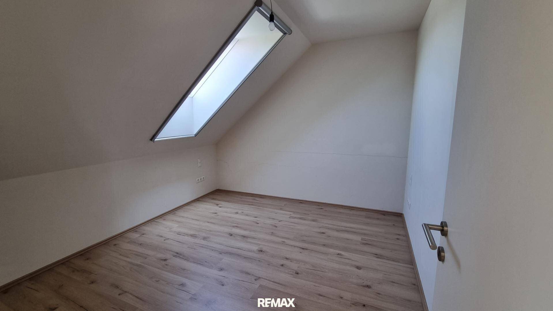 Schlafzimmer mit hellem Laminatboden, weißen Wänden und einem Dachfenster, das den Raum mit Licht füllt.