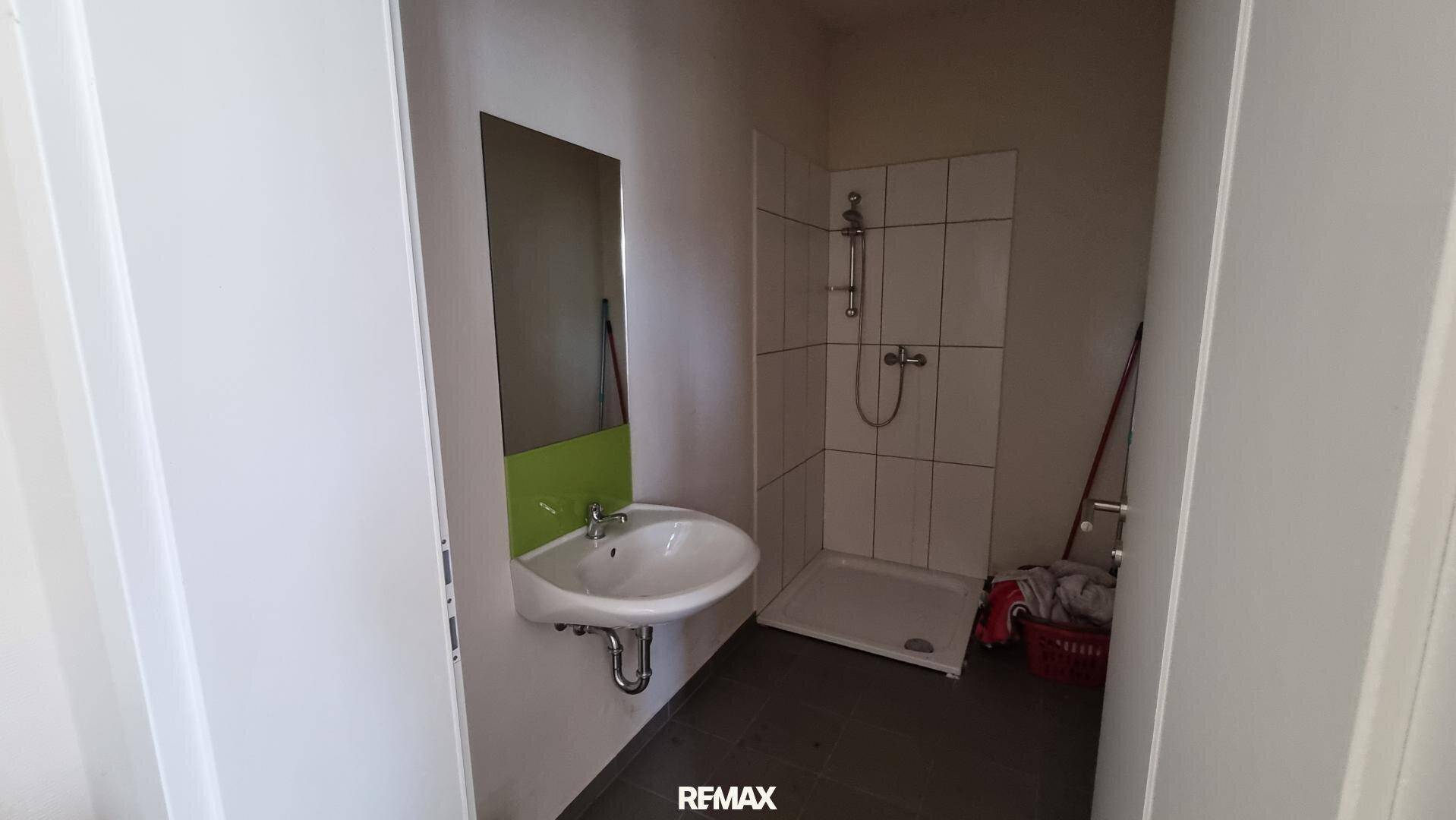 Badezimmer mit Duschkabine, Waschbecken und Spiegel, einfach und funktional eingerichtet.