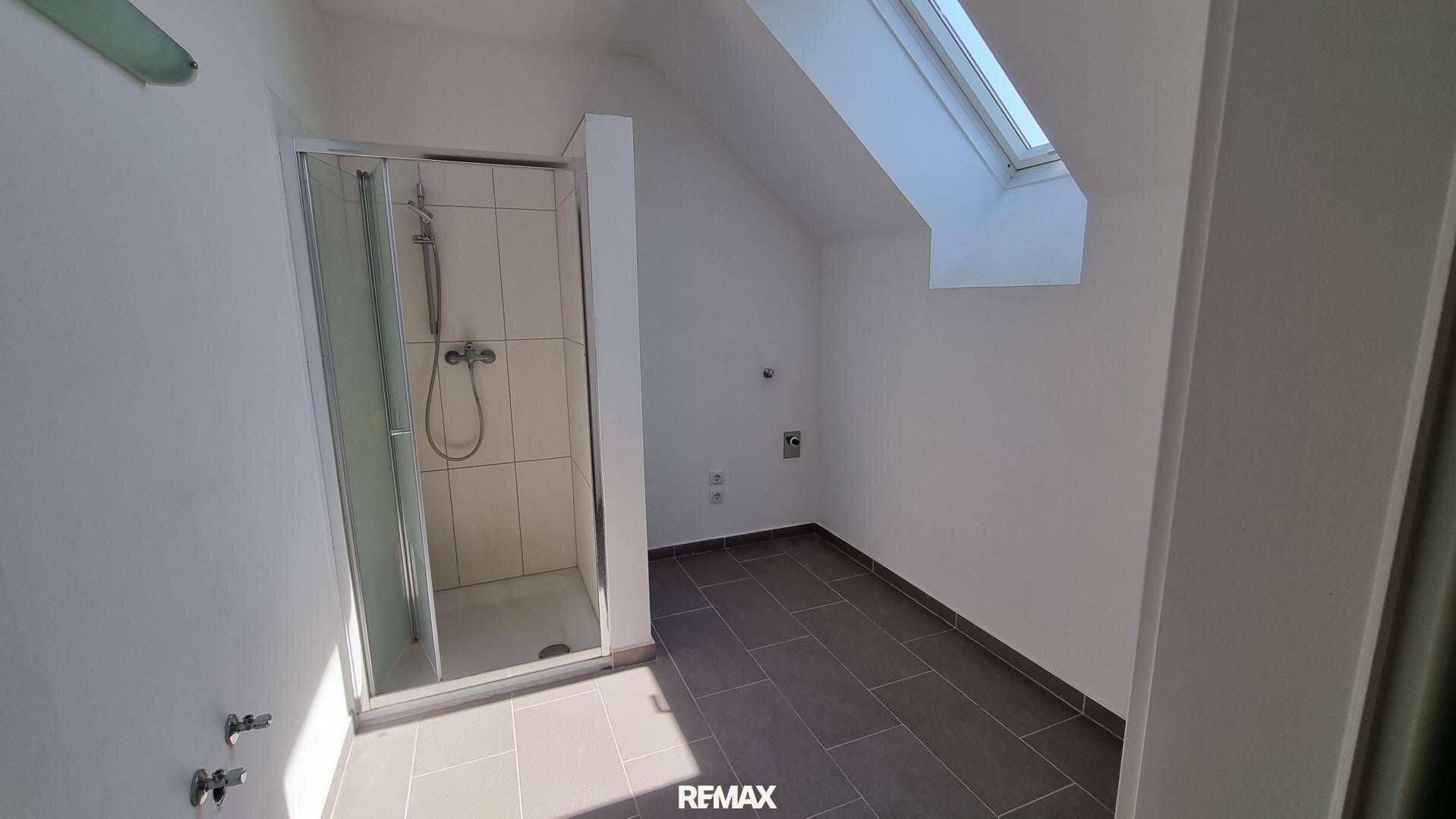 Badezimmer mit Duschkabine, dunklen Bodenfliesen und einem Dachfenster, das für natürliches Licht sorgt.