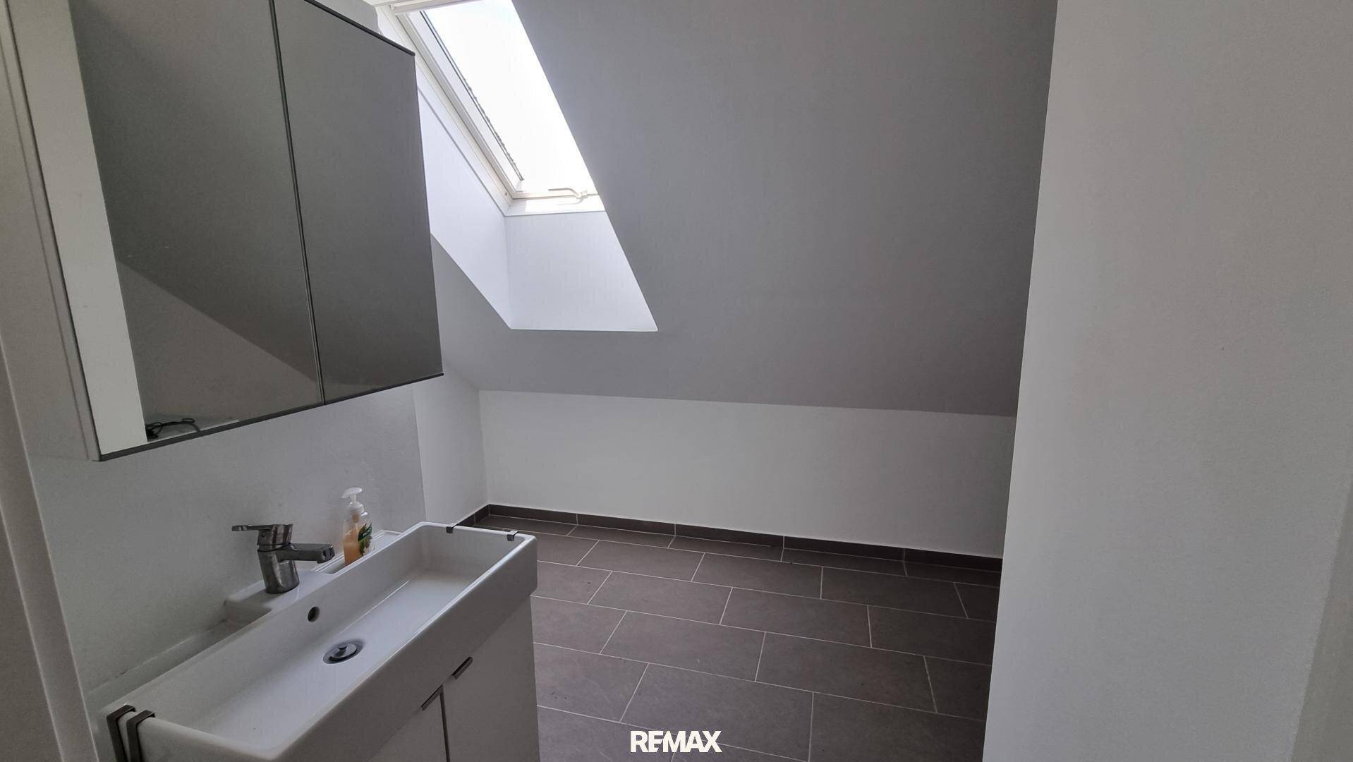 Badezimmer im Dachgeschoss mit schräger Decke, Dachfenster, Waschbecken und Spiegelschrank.