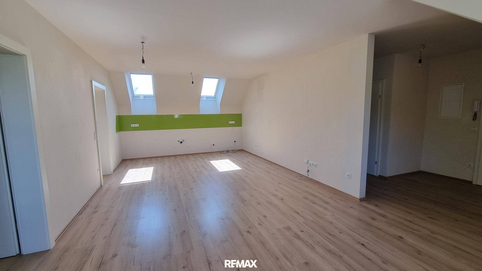 Weiterer Blick auf den großen offenen Raum mit Laminatboden, Dachfenstern und einer grünen Wandakzentuierung.