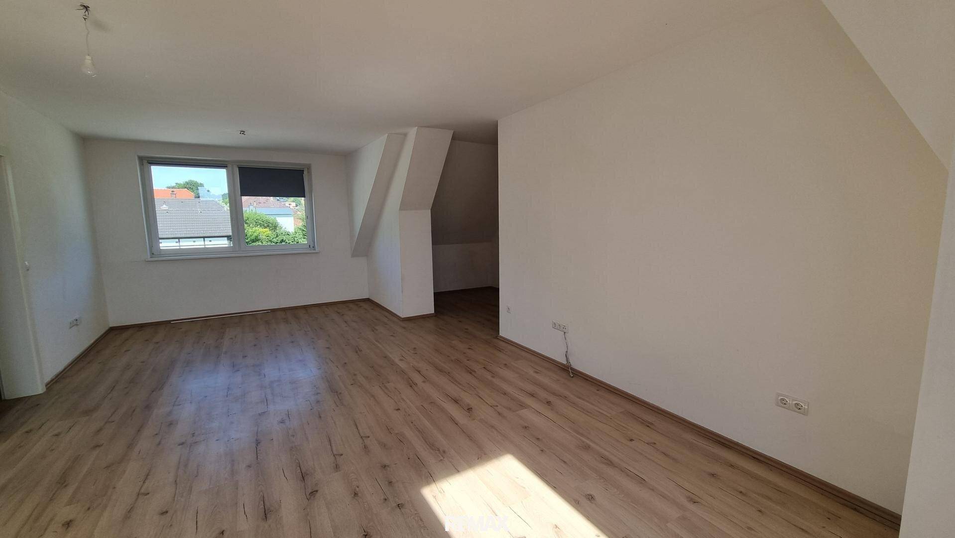 Großer Raum mit hellem Laminatboden und weißen Wänden, ausgestattet mit einem Fenster für Tageslicht.