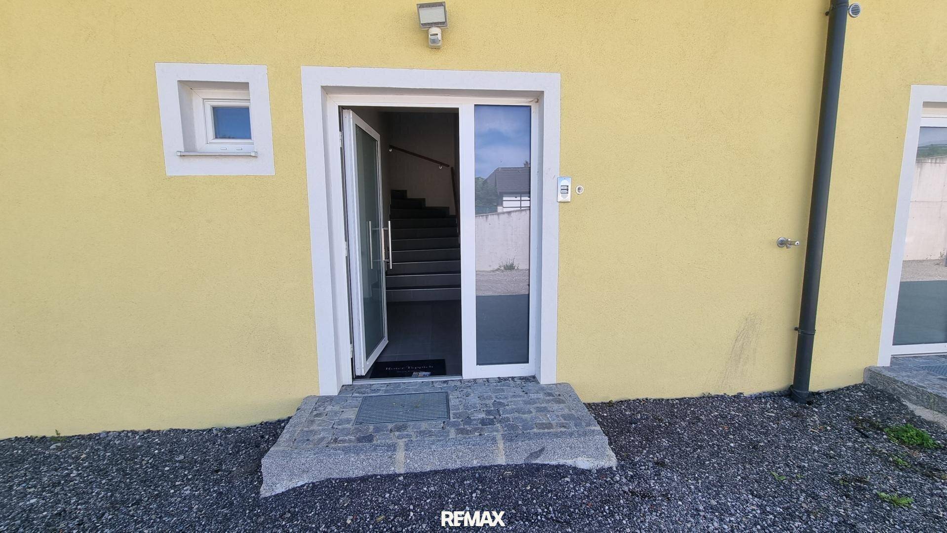Nahaufnahme eines Haupteingangs mit Glastür, die zu einer Treppe im Inneren des Gebäudes führt.