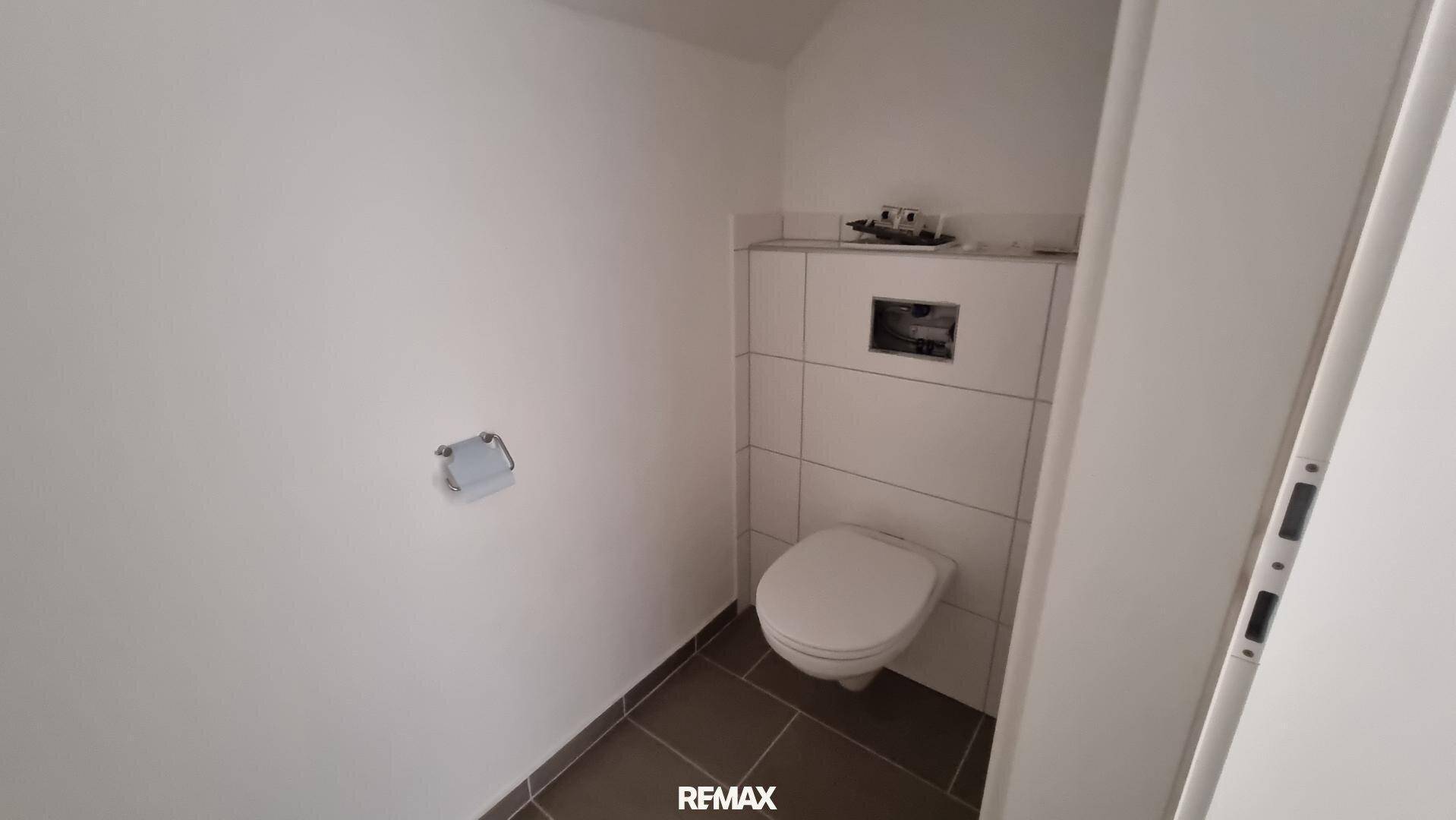 Kleiner Toilettenraum mit wandhängendem WC und dunklen Bodenfliesen, in einem modernen Stil gehalten.