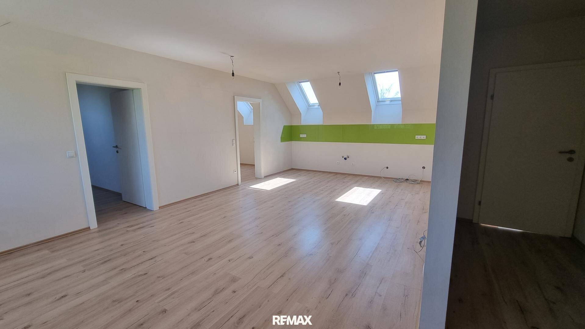 Großer offener Raum mit Laminatboden, weißen Wänden und Dachfenstern, ideal für Wohnen und Kochen.