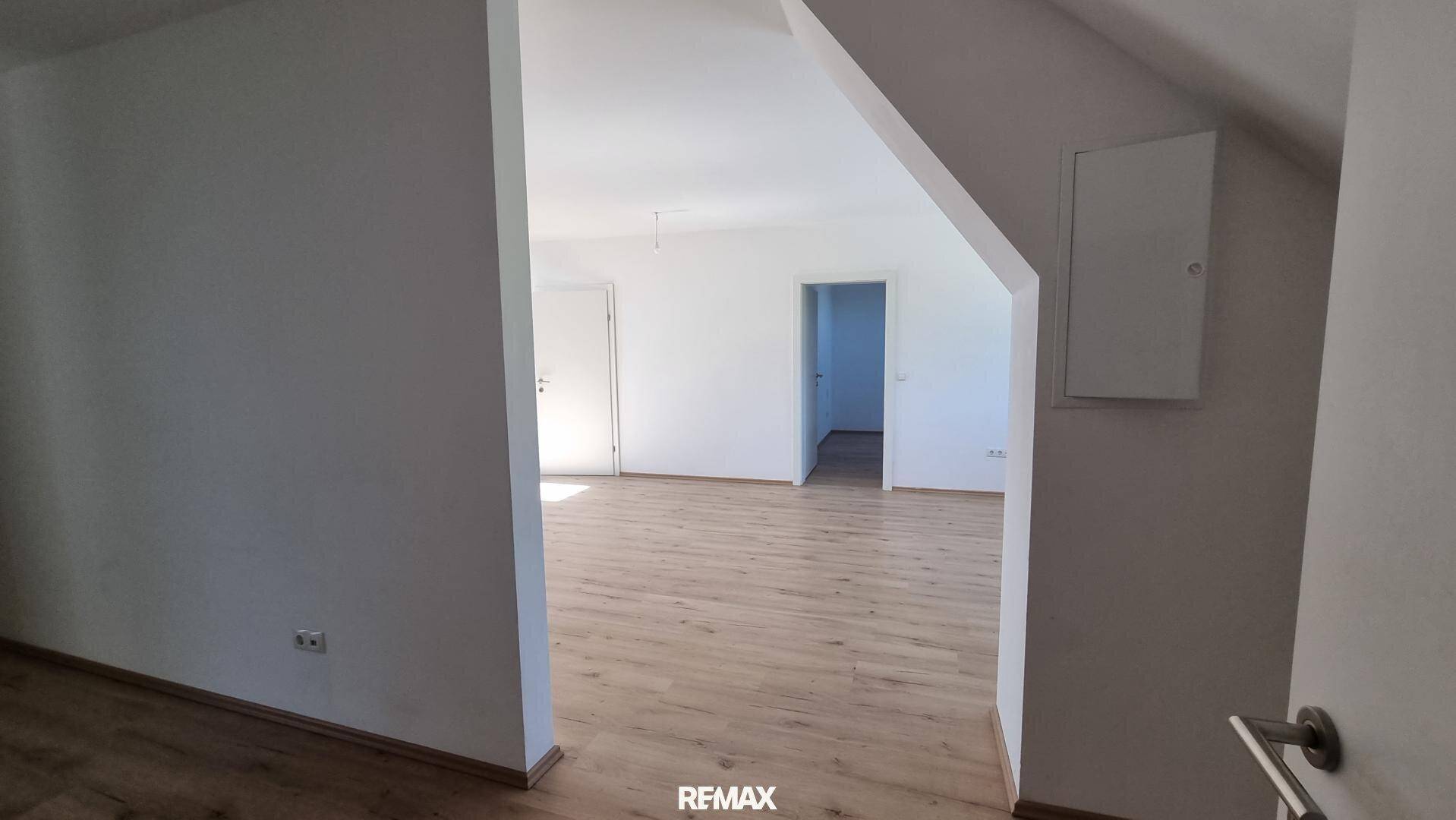 Heller Wohnraum mit hellem Laminatboden und weißen Wänden, der zu einem weiteren Zimmer führt.