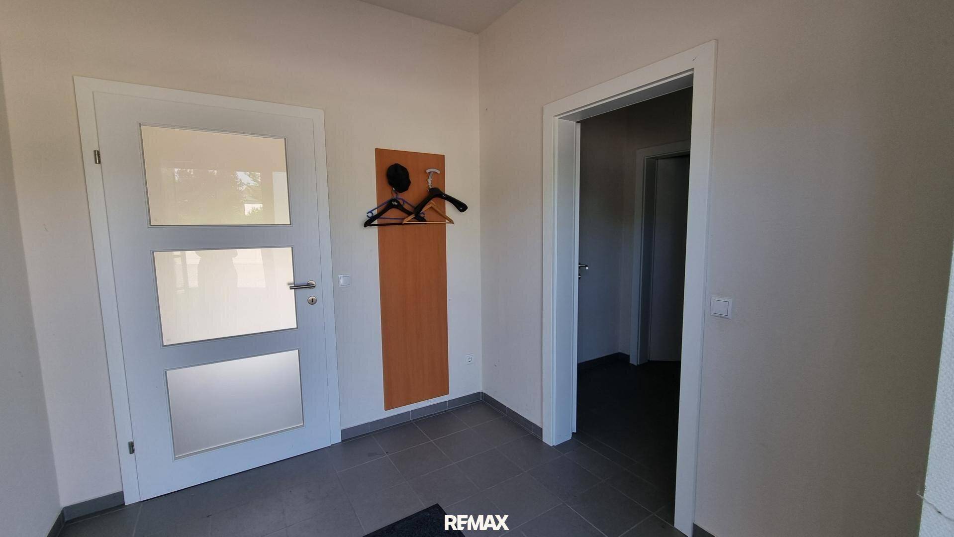Eingangsbereich mit Fliesenboden, Garderobe und modernen Türen mit Glaseinsätzen, hell und einladend.