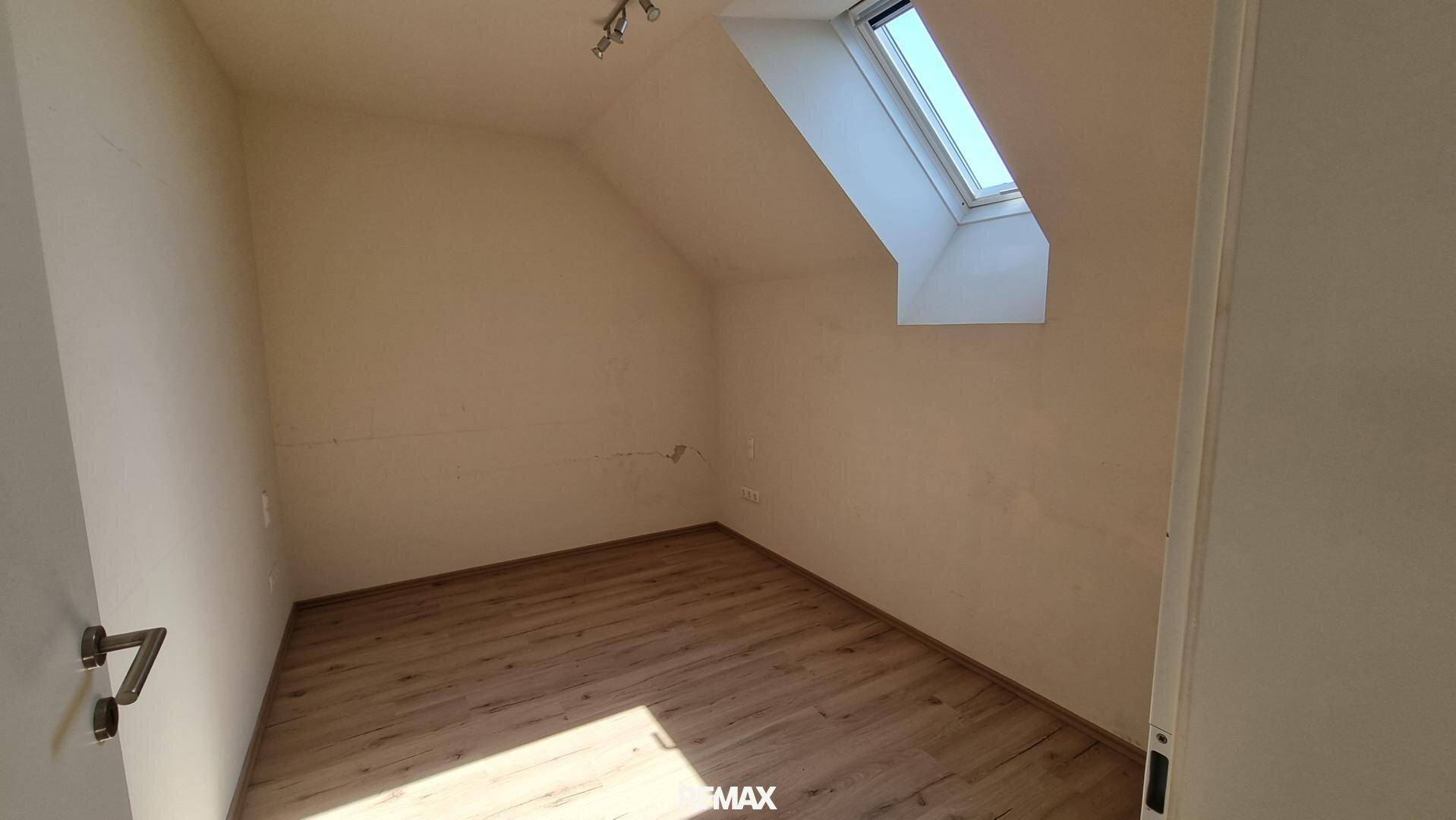 Helles Schlafzimmer mit Laminatboden, weißen Wänden und einem Dachfenster, das für eine freundliche Atmosphäre sorgt.