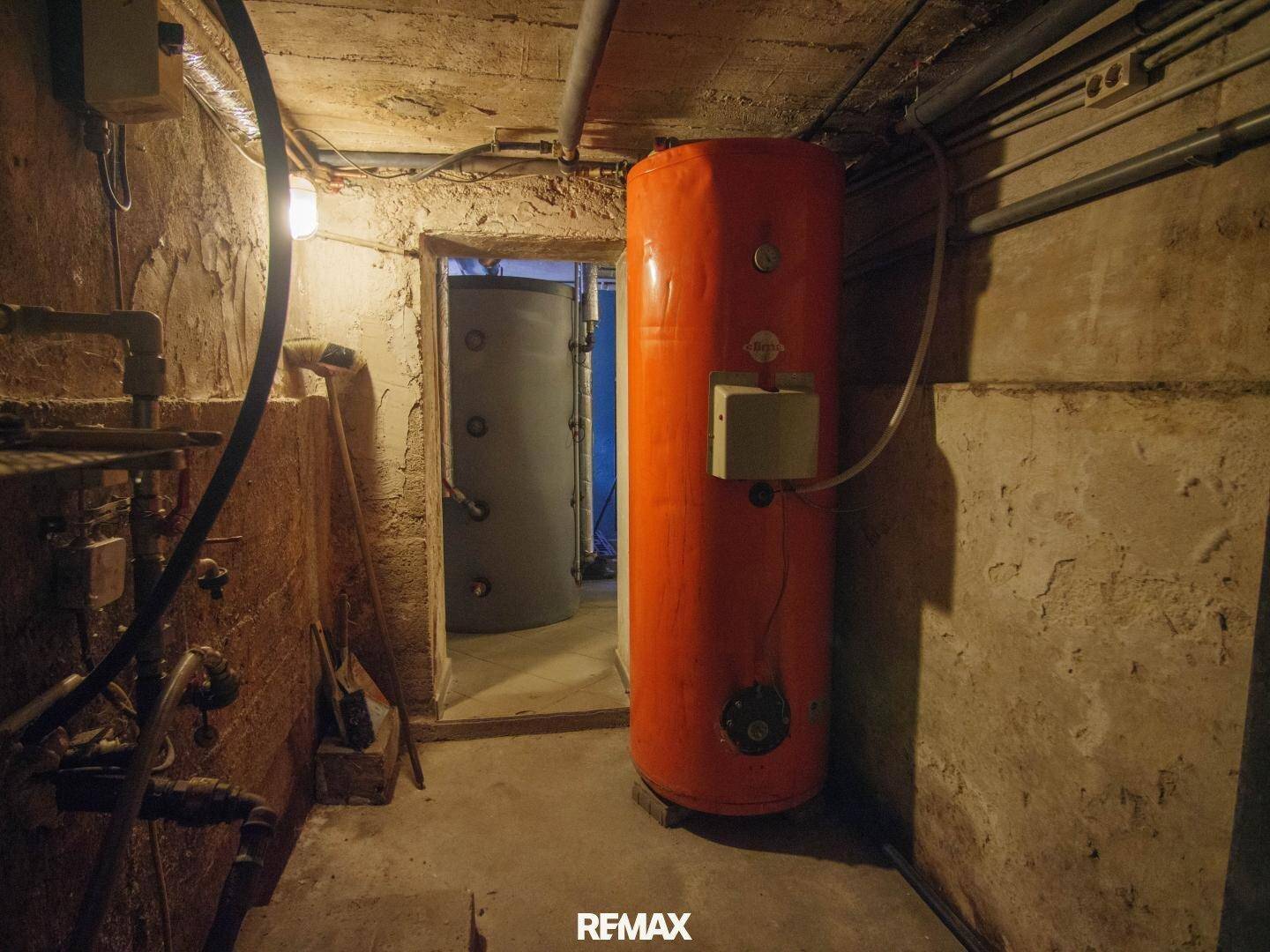 Kellerraum mit großem orangefarbenem Warmwasserspeicher und sichtbaren Installationen.