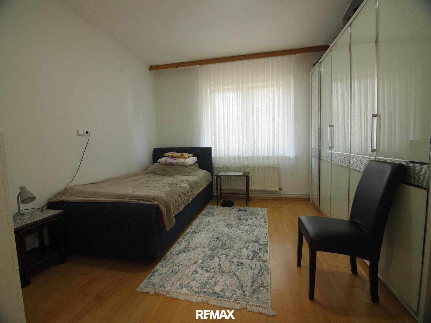 Schlafzimmer mit Einzelbett, Kleiderschrank und hellem Laminatboden, gut beleuchtet.