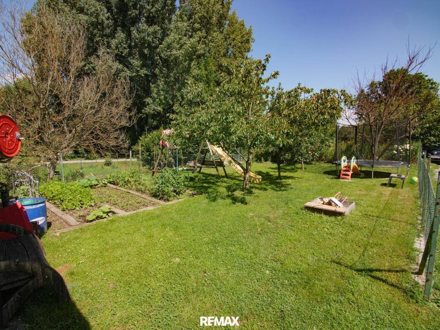 Großer Garten mit Rasenfläche, Obstbäumen, Sandkasten und Trampolin für Kinder.