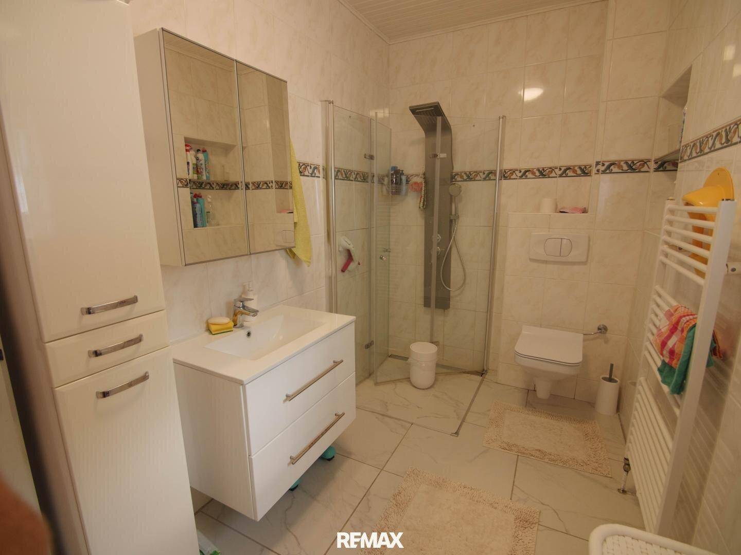 Modern gefliestes Badezimmer mit Duschkabine, wandhängendem WC und Waschtisch mit Spiegelschrank.