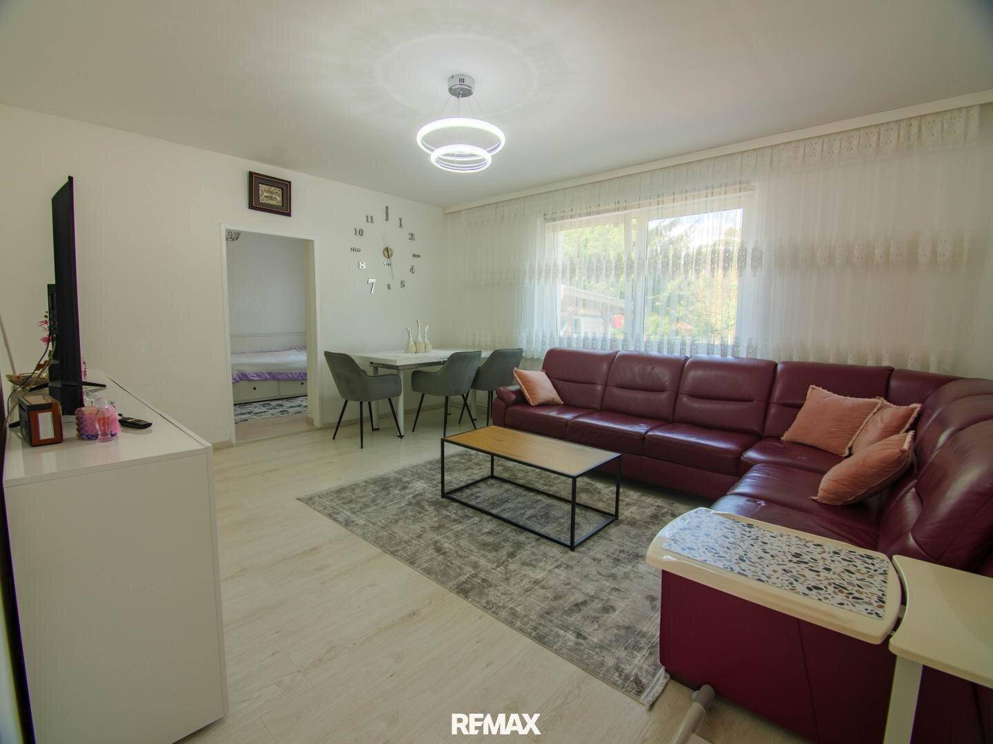 Geräumiger Wohn-Essbereich mit rotem Ledersofa, Esstisch und hellem Laminatboden.