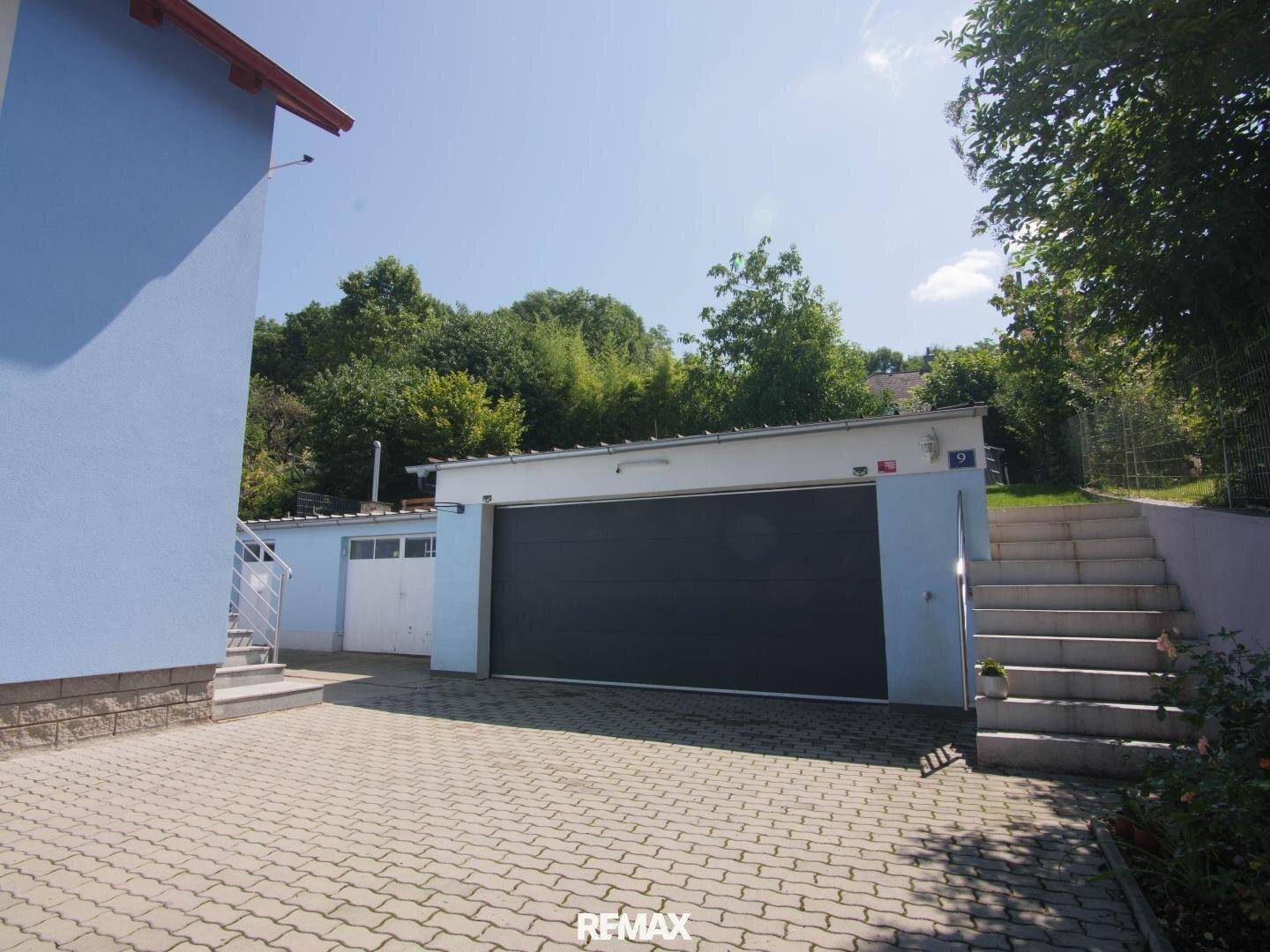 Geräumige Garage mit großem Tor und gepflasterter Zufahrt, umgeben von Grün.