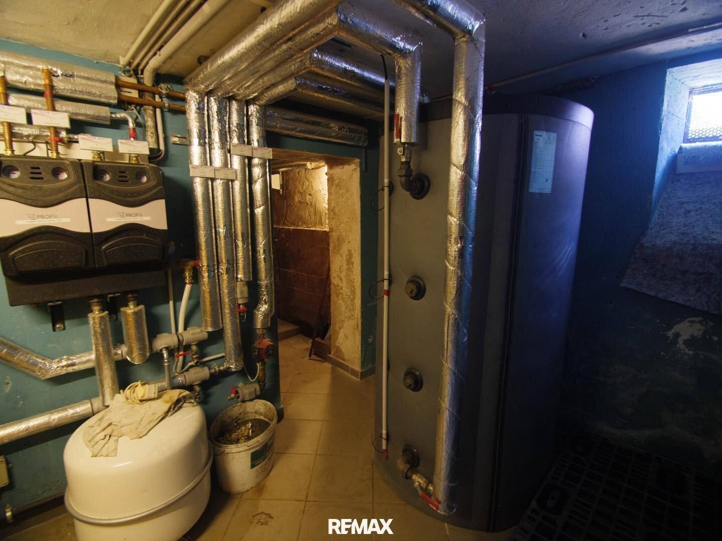 Technikraum im Keller mit Heizungsanlage, Warmwasserspeicher und zahlreichen Rohrleitungen.