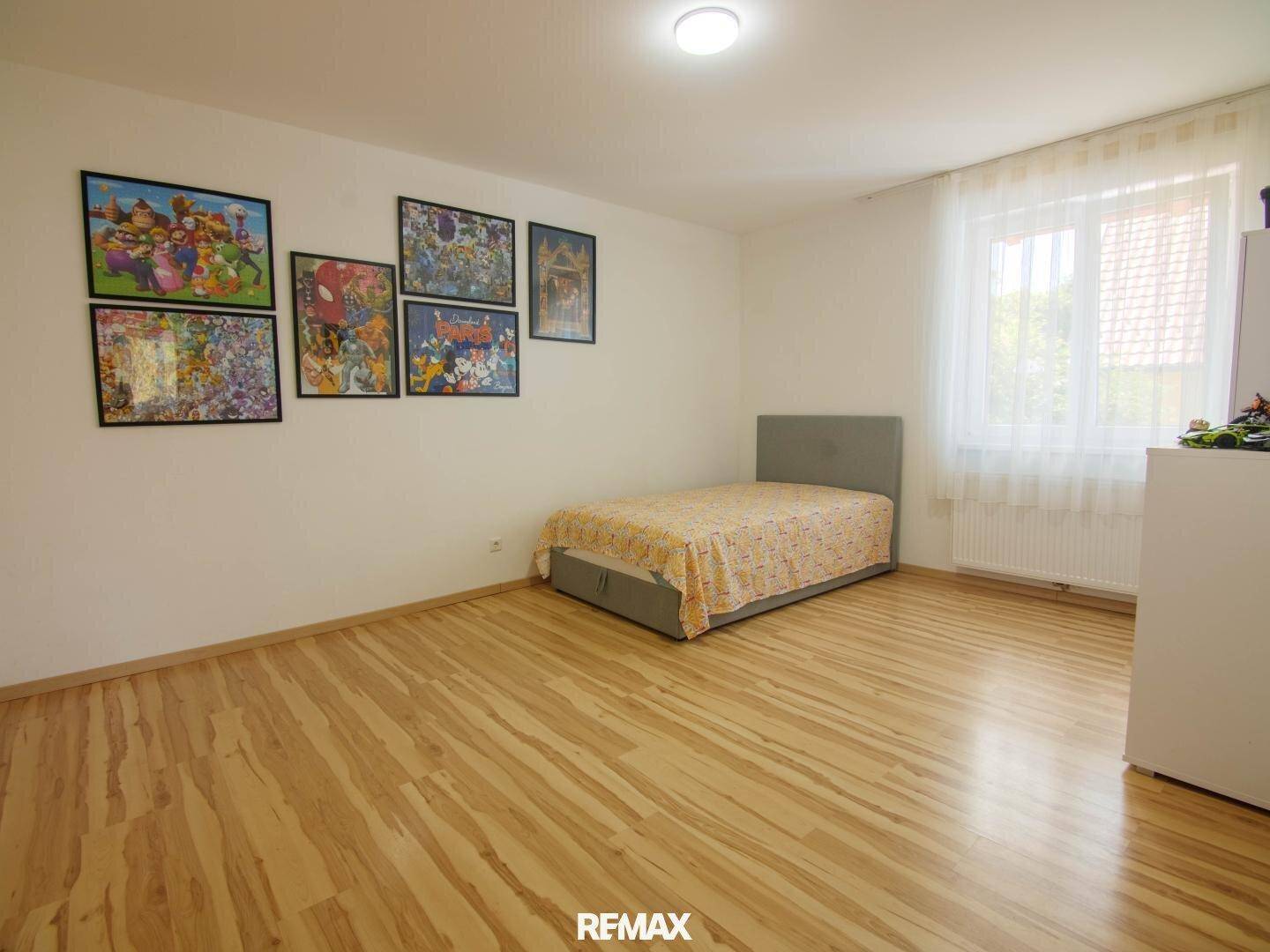 Helles Schlafzimmer mit Einzelbett, Laminatboden und farbenfrohen Bildern an der Wand.