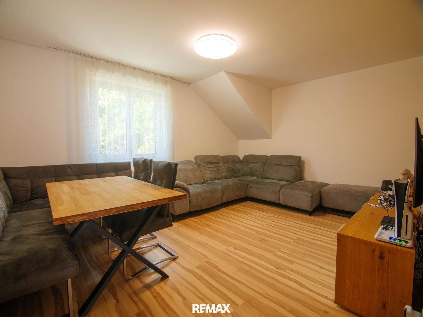 Gemütliches Wohnzimmer mit Ecksofa, Holztisch und hellem Laminatboden unter Dachschräge.