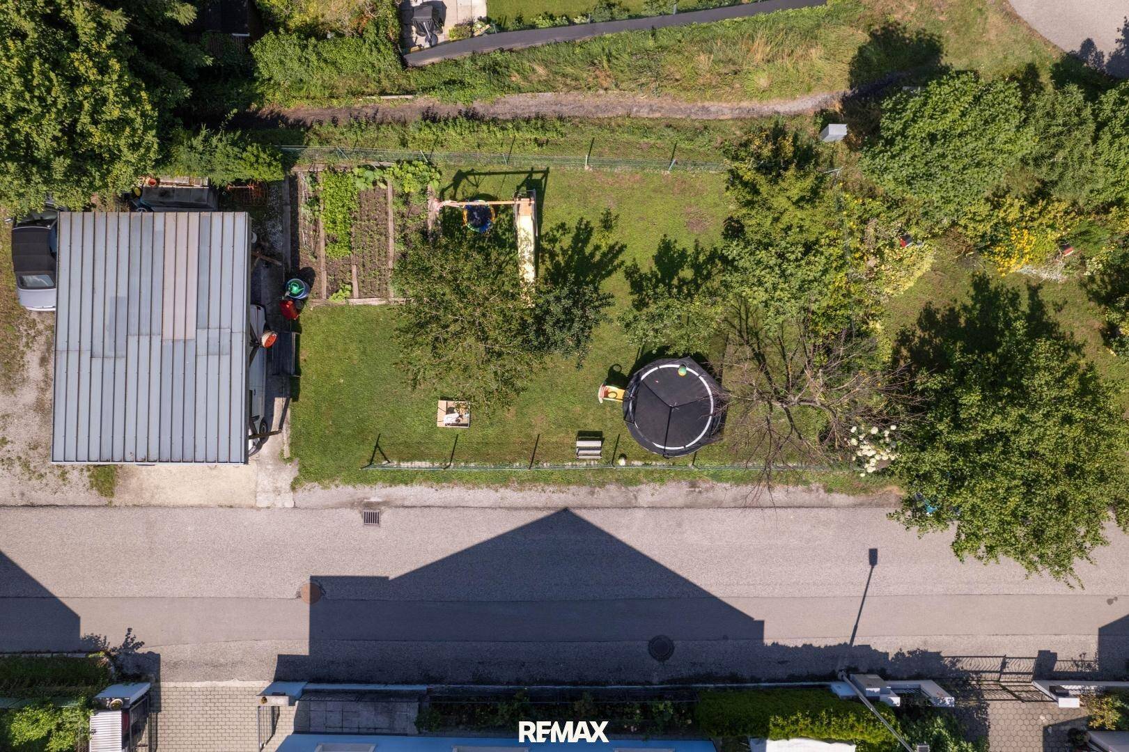 Gartenbereich mit Trampolin, kleinem Gemüsegarten und einem überdachten Stellplatz.