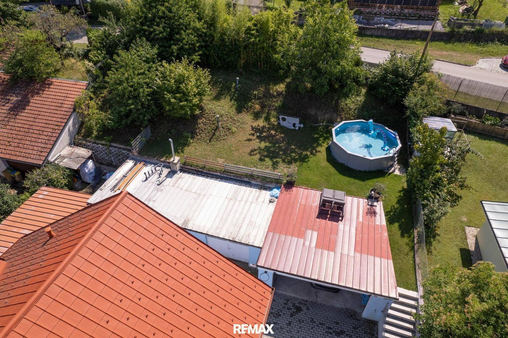 Luftaufnahme des Hauses mit rotem Dach, großer Terrasse und einem Aufstellpool im Garten.