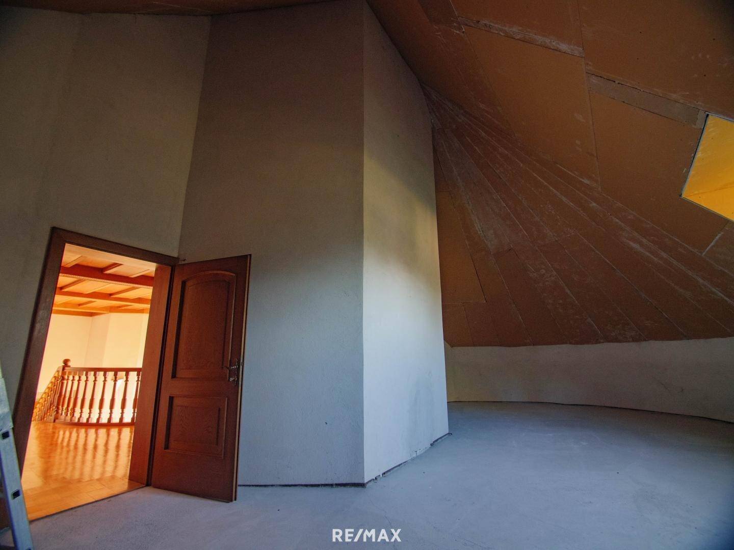 Unausgebauter Dachbodenbereich mit schrägen Wänden und Holztür.