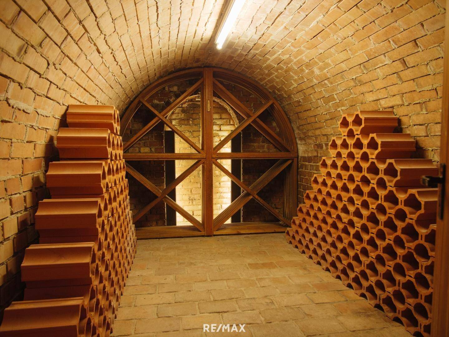 Gewölbter Weinkeller mit Ziegelwänden, Flaschenregalen und traditioneller Holztür.