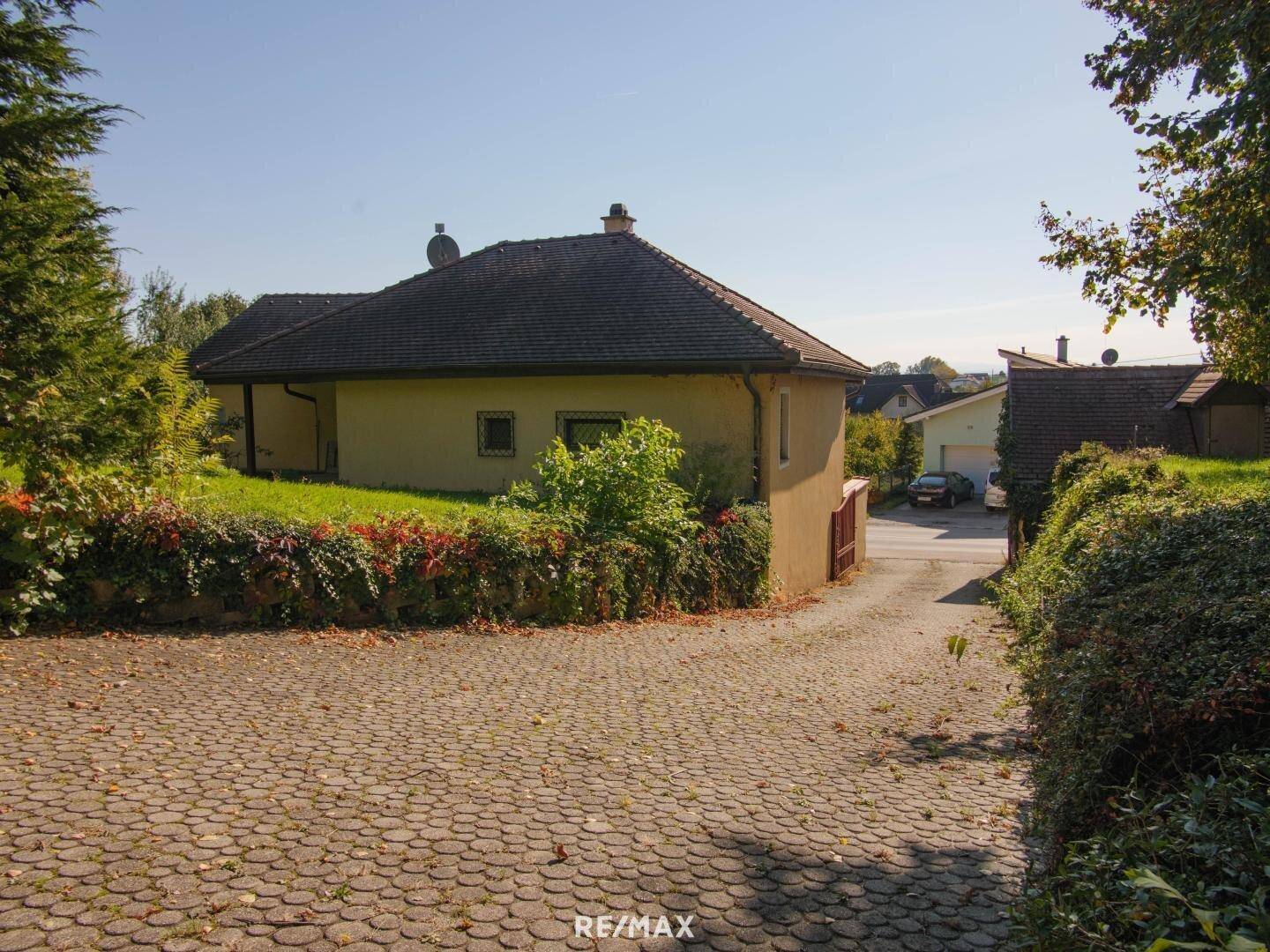 Seitenansicht des Hauses mit gepflasterter Zufahrt und grüner Bepflanzung.