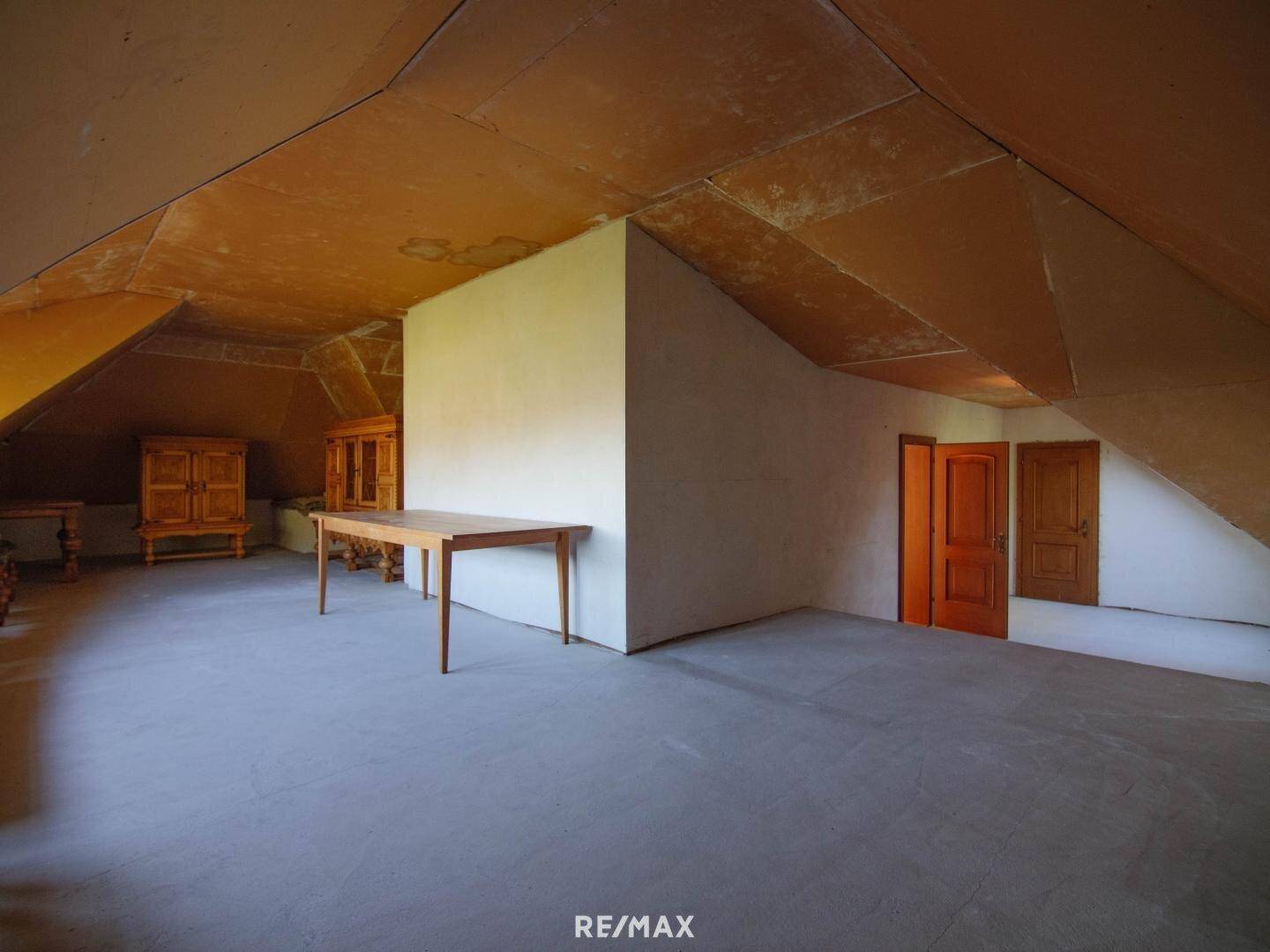 Großer unausgebauter Dachboden mit schrägen Wänden und Holztisch.