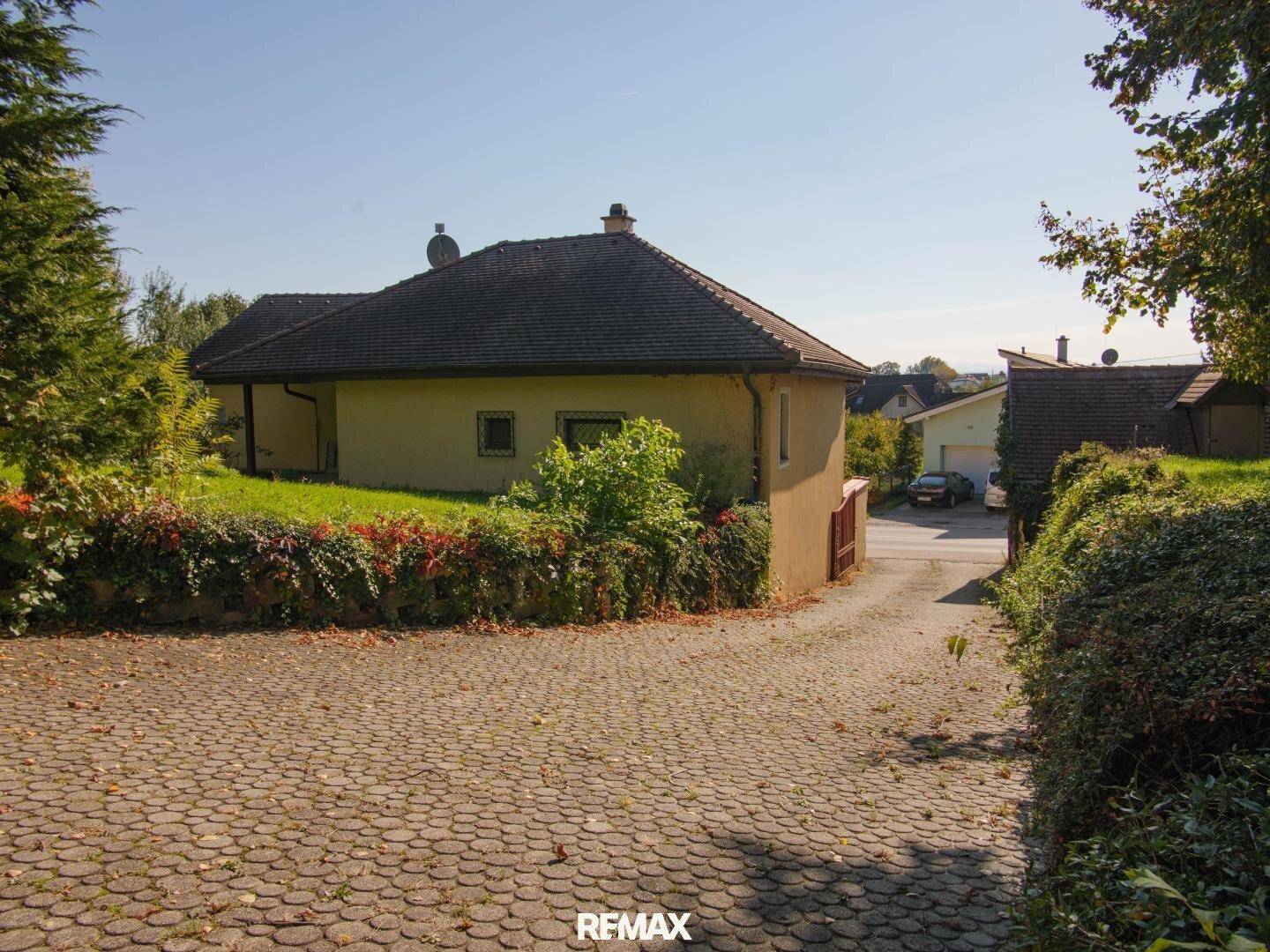 Ansicht des Hauses von der gepflasterten Auffahrt, umgeben von Grünflächen.
