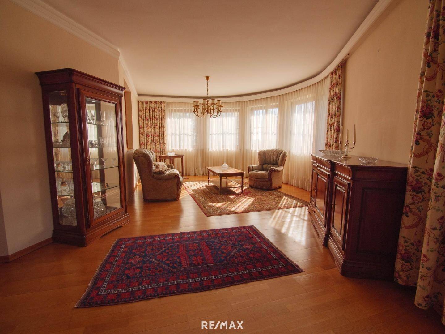 Geräumiges Wohnzimmer mit Holzboden, traditionellen Möbeln und vielen Fenstern.