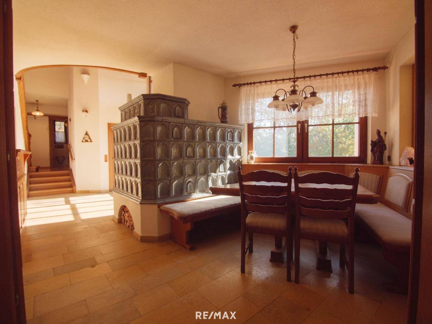 Heller Essbereich mit Kachelofen, Holzbänken und Blick in den Garten.