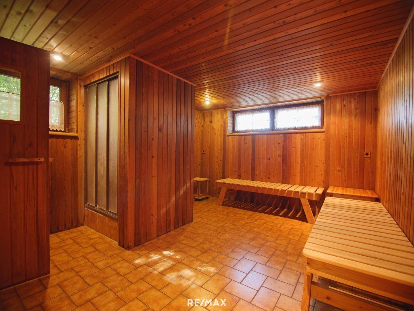 Geräumiger Wellnessbereich mit Holzverkleidung, Bänken und separater Duschkabine.