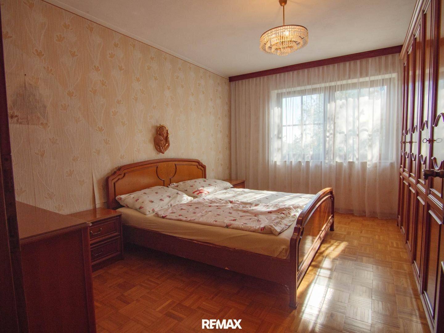 Schlafzimmer mit Doppelbett, Holzmöbeln, gemusterter Tapete und Parkettboden.