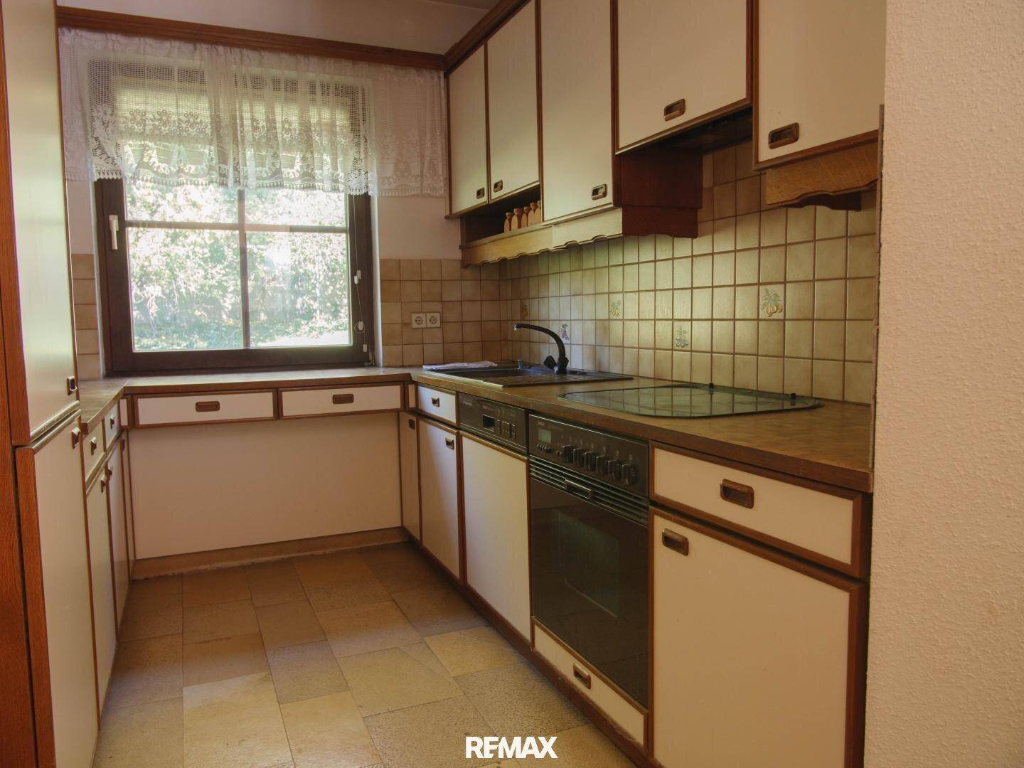 Funktionale Küche mit weißen und braunen Schränken, gefliestem Spritzschutz und Fenster.