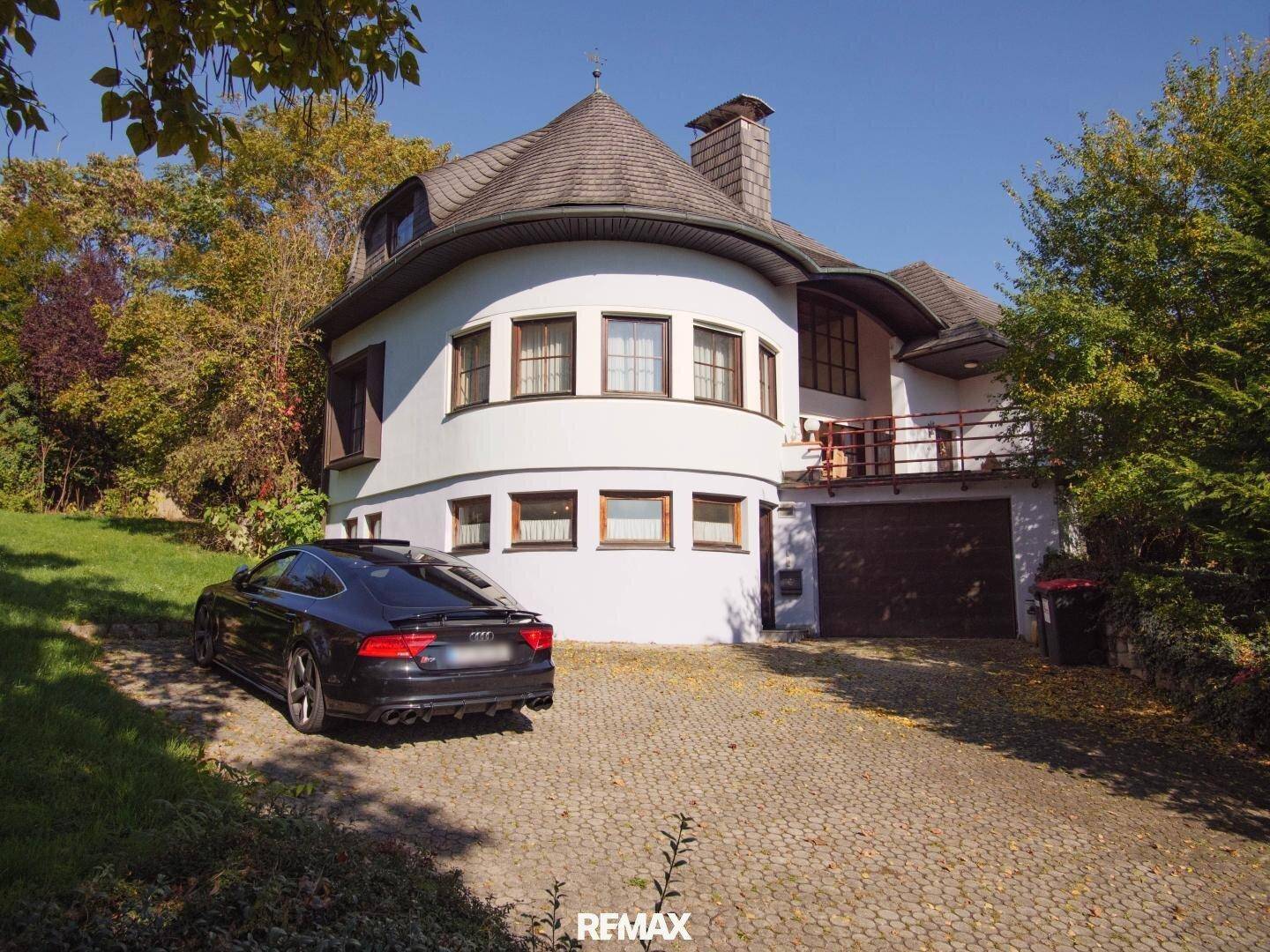 Ansicht des Hauses mit geschwungener Fassade, gepflasterter Auffahrt und integrierter Garage.