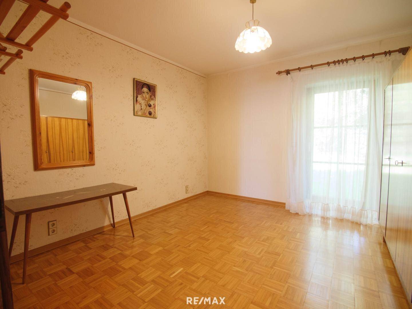 Leeres Schlafzimmer mit Parkettboden, Fenster und einfacher Einrichtung.