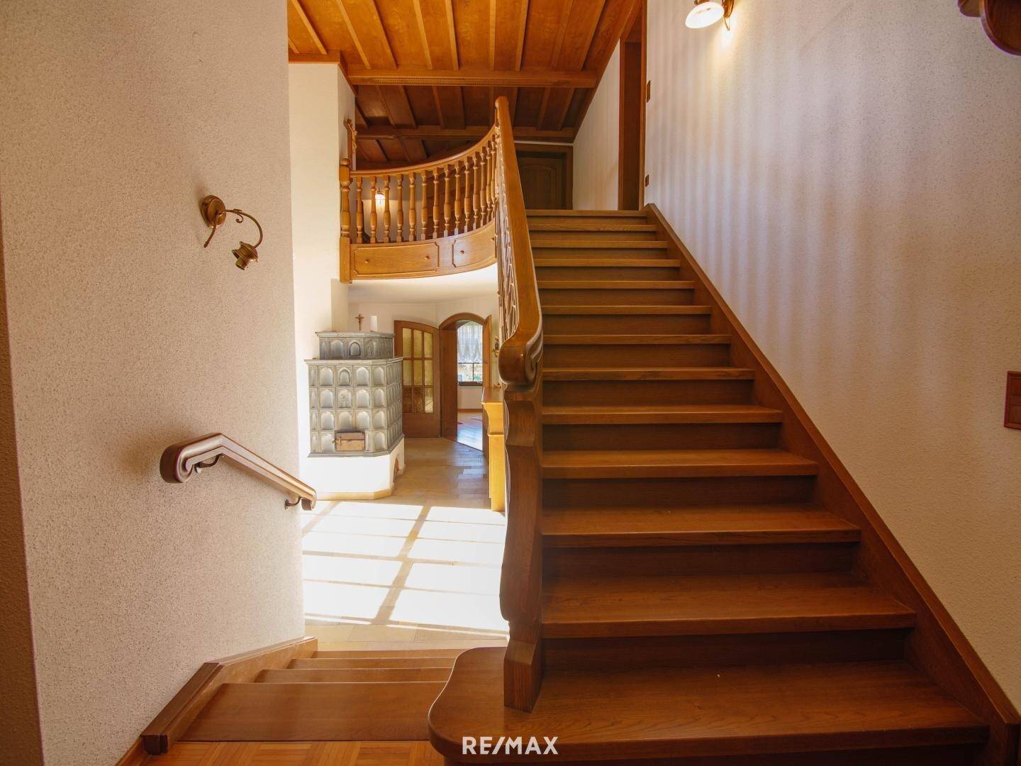 Holztreppe führt zu den oberen Etagen, mit Kachelofen im Hintergrund.
