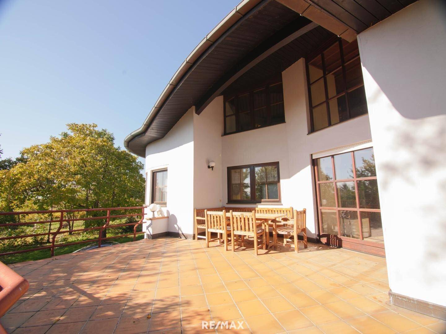 Große Sonnenterrasse mit Terrakotta-Fliesen, Holztisch und Blick ins Grüne.