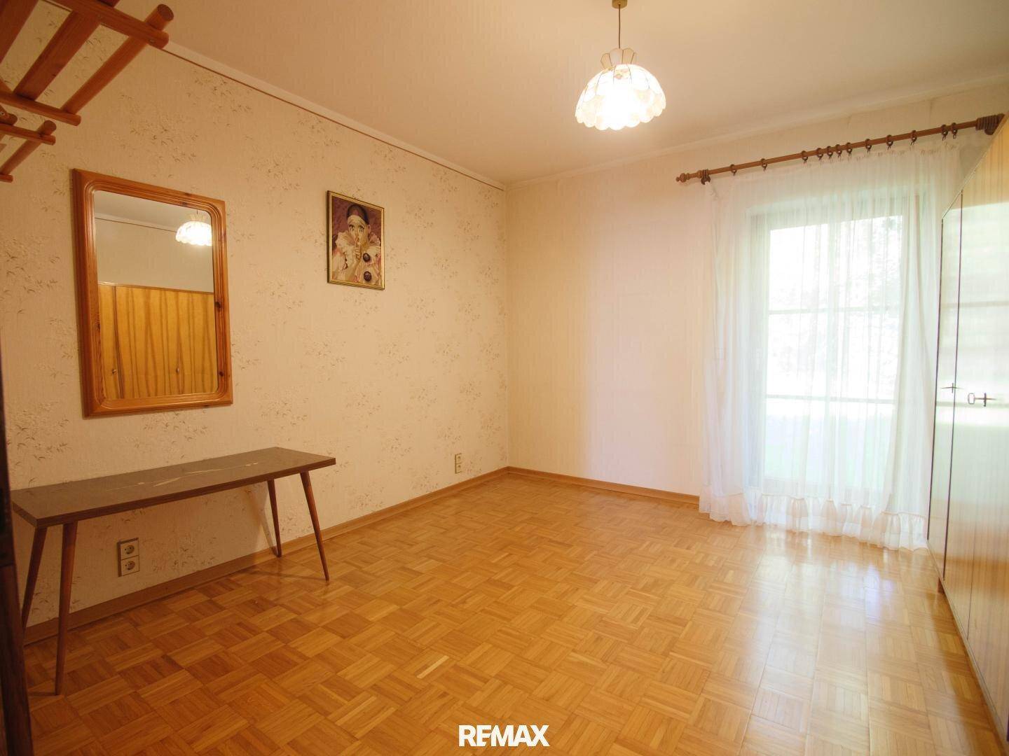 Leeres Schlafzimmer mit Parkettboden, gemusterter Tapete und einem Fenster.