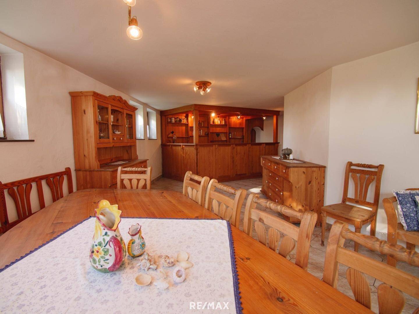 Großer Essbereich im Keller mit Holztischen, Stühlen und einer Bar im Hintergrund.