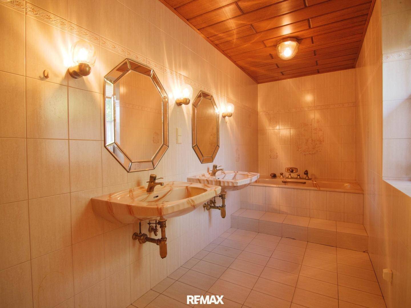 Badezimmer mit Doppelwaschbecken, eingebauter Badewanne, gefliesten Wänden und Holzdecke.