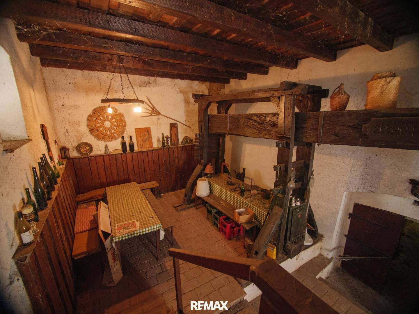 Rustikaler Weinkeller mit historischer Weinpresse, Holzbalken und Flaschenregalen.