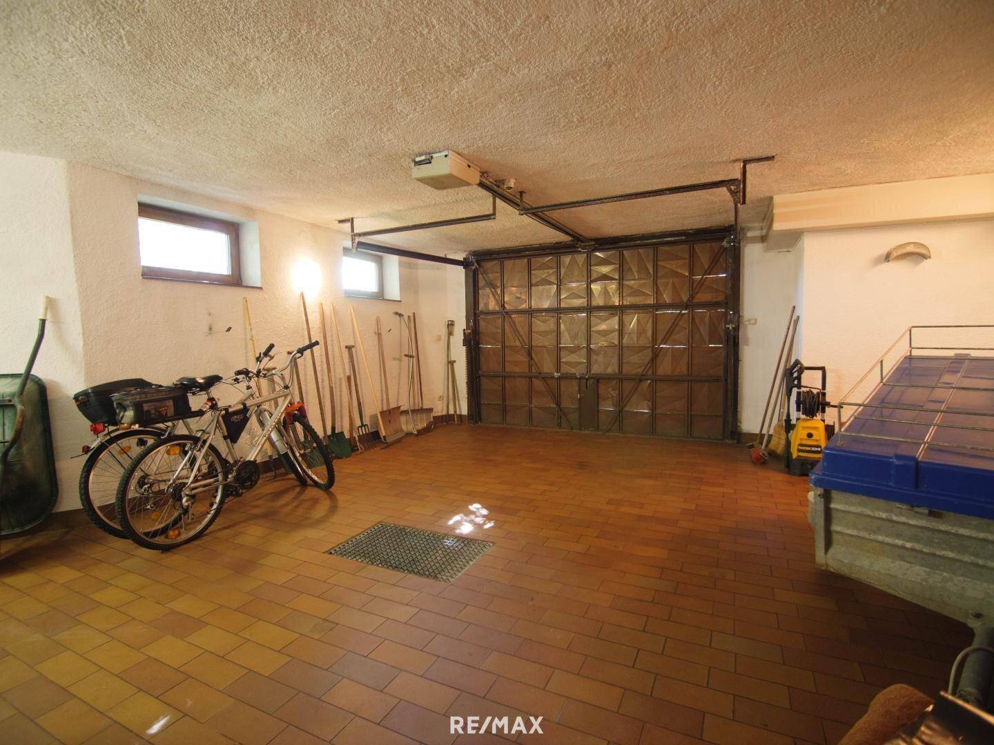 Geräumige Garage mit Fliesenboden, Fenstern und Platz für Fahrräder.