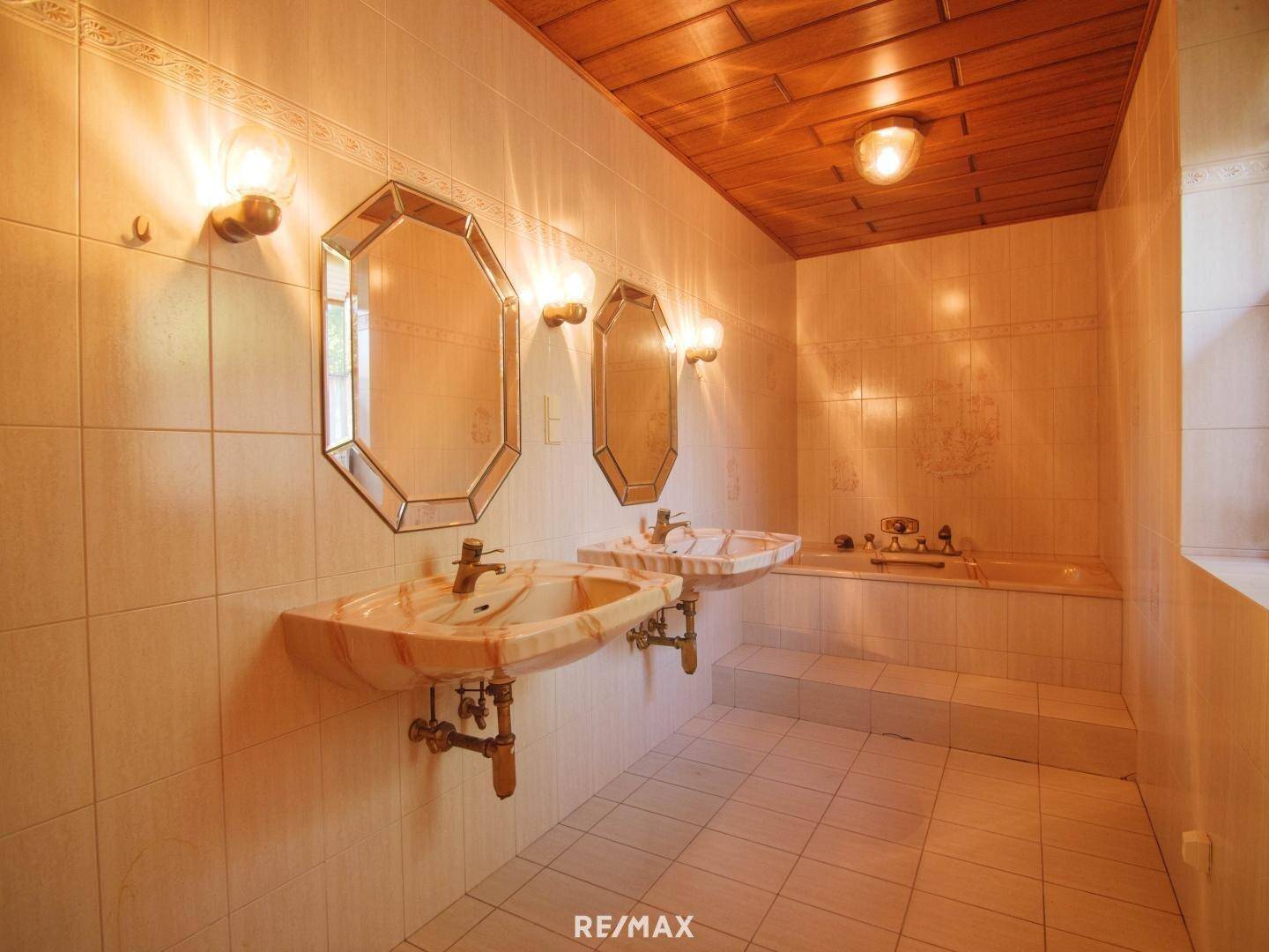 Badezimmer mit Doppelwaschbecken, Badewanne, Fliesen und Holzdecke.