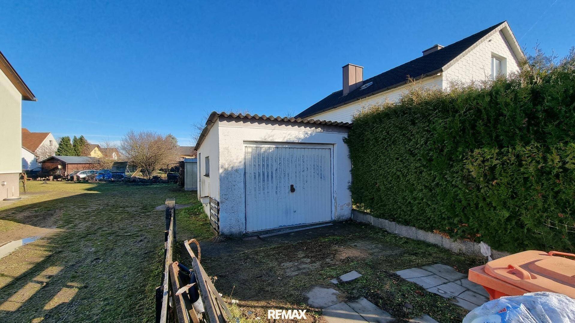 Freistehende Garage mit Schwingtor und angrenzendem Gartenbereich.