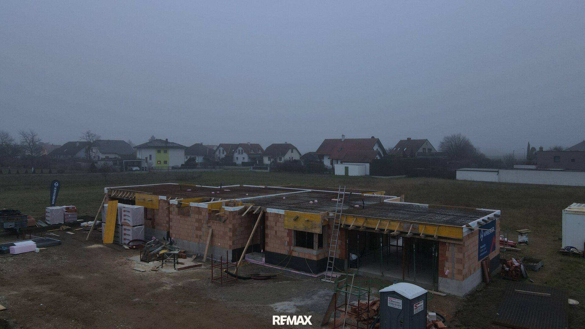 Luftaufnahme einer Baustelle im Rohbau an einem nebligen Tag mit ländlicher Umgebung.