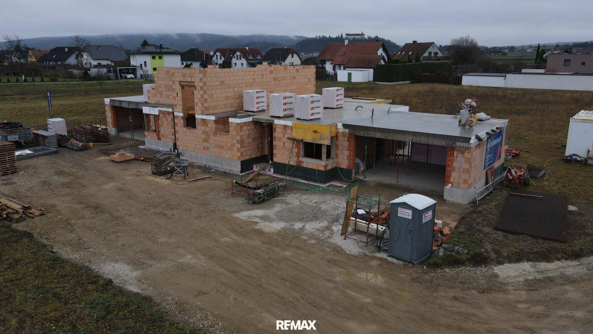 Luftaufnahme einer Baustelle mit Rohbau und vorbereiteter Dachkonstruktion.