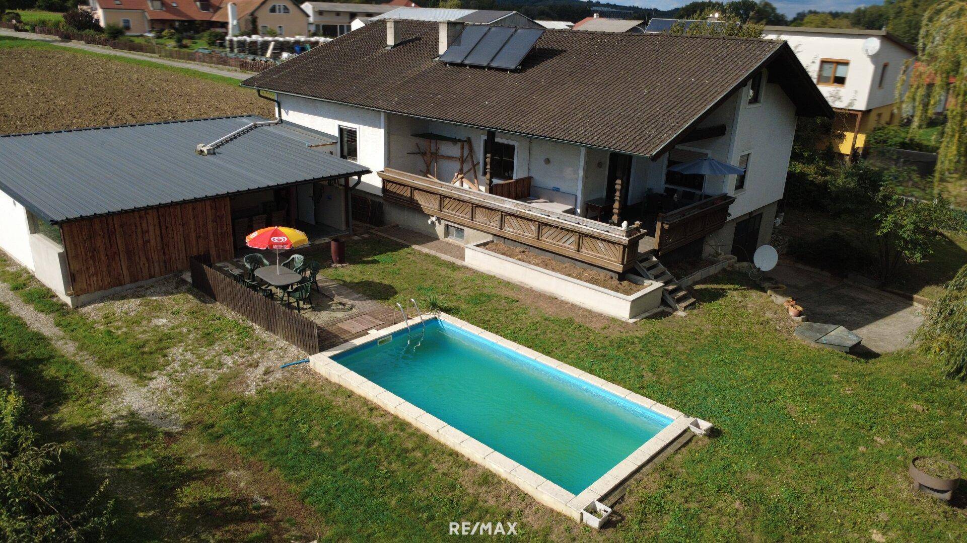 Hinterhof mit Swimmingpool, Terrasse und Gartenmöbeln, umgeben von grüner Landschaft.