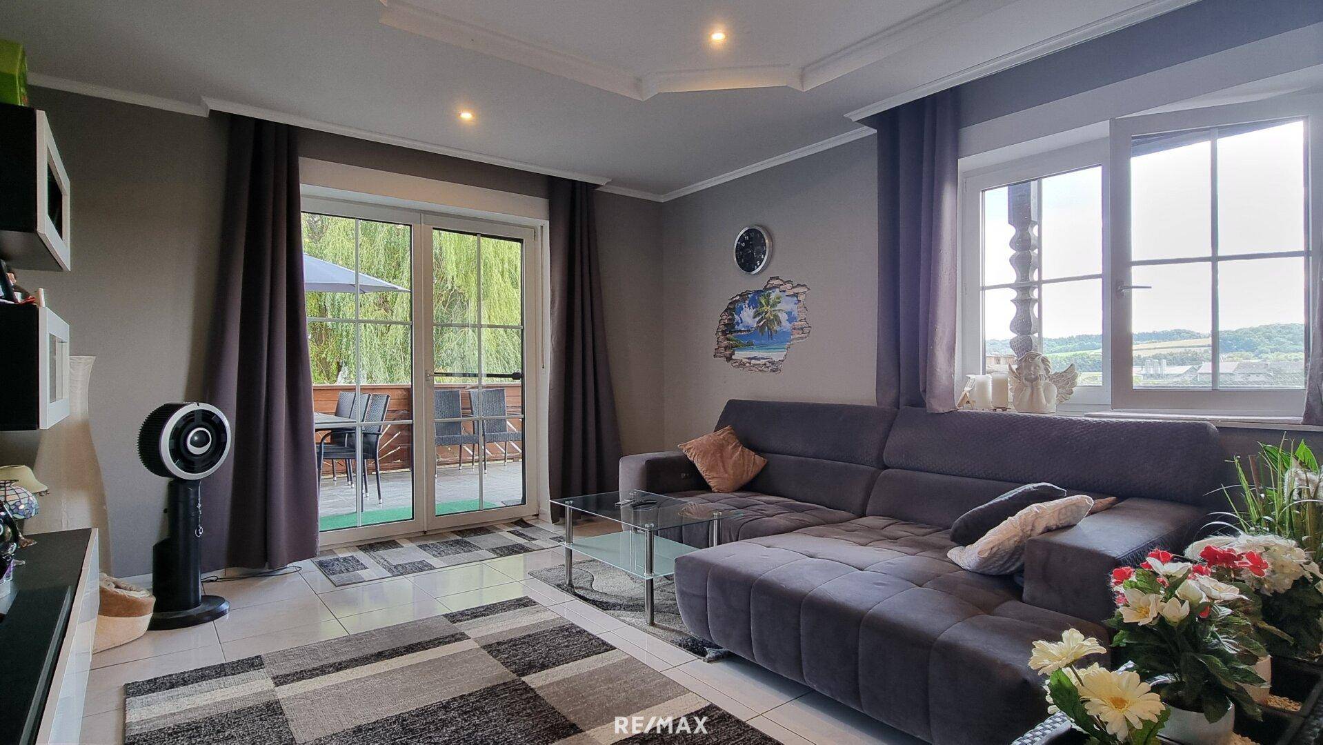 Gemütliches Wohnzimmer mit großem Sofa, Fliesenboden und Zugang zur Terrasse.