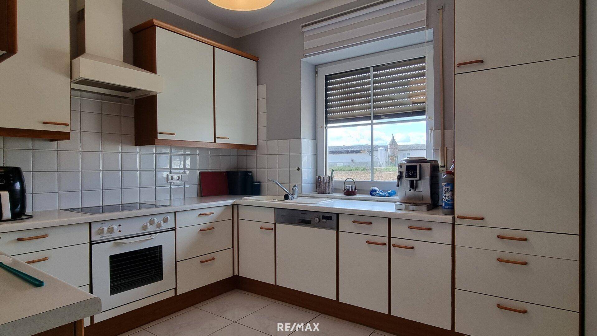 Funktionale Küche mit weißen Schränken, Fliesenrückwand und Fenster mit Blick ins Grüne.