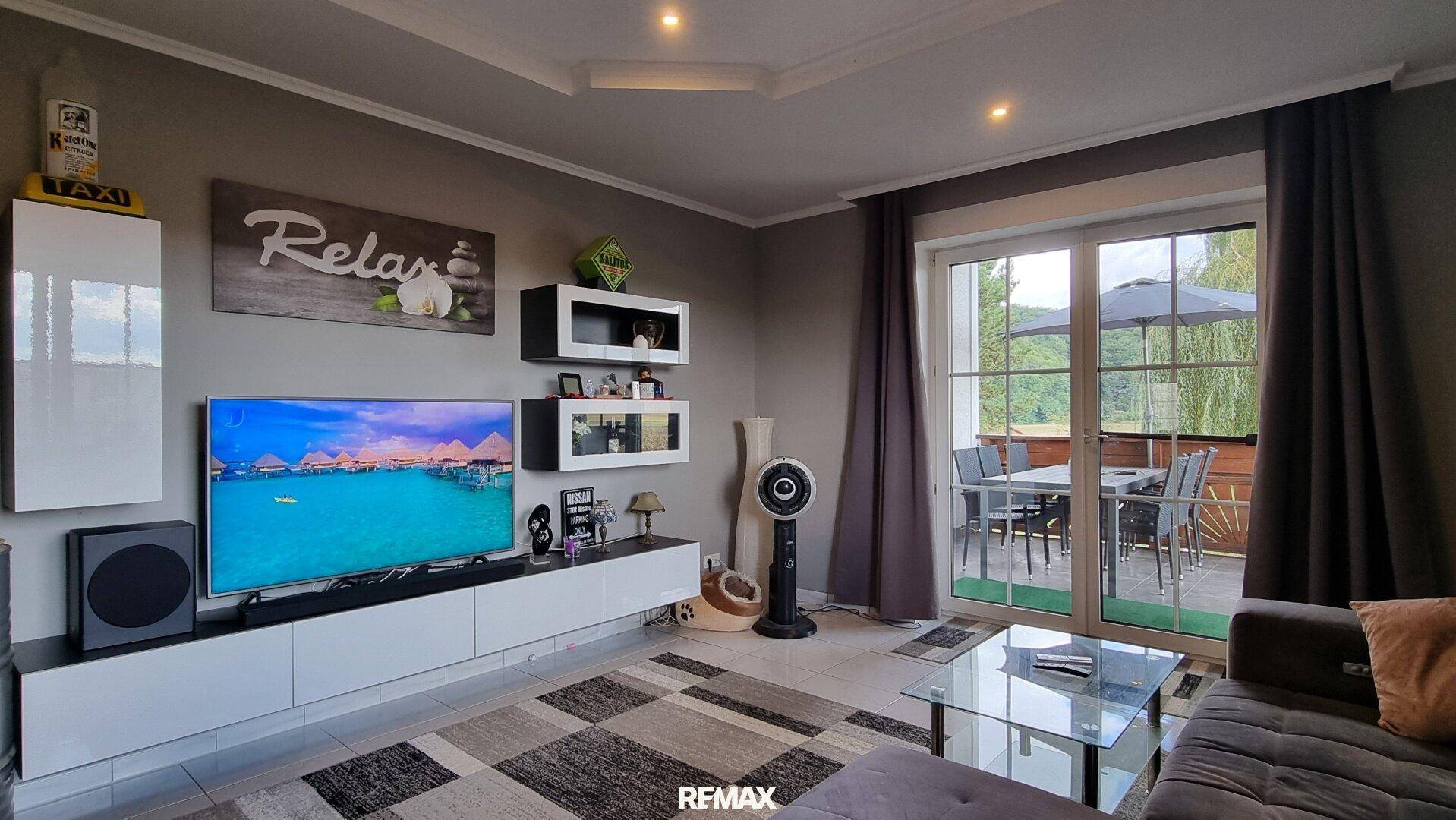 Wohnzimmer mit großem Fernseher, modernen Möbeln und direktem Zugang zur Terrasse.